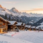 Vue d’un village alpin chic avec chalets en bois, montagnes enneigées et éclairage chaleureux dans une ambiance immobilière haut de gamme.
