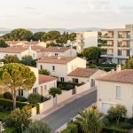 Vue réaliste d’un quartier résidentiel du Crès avec des maisons méditerranéennes, des immeubles récents, des rues arborées et une lumière douce.